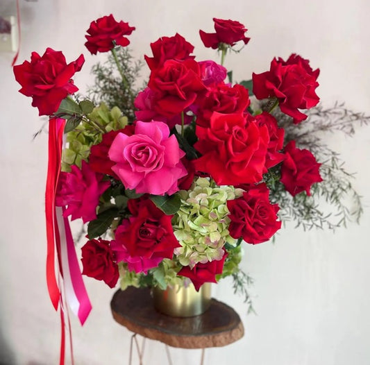 Bouquet of red and pink roses with green hydrangeas on a wooden stool.