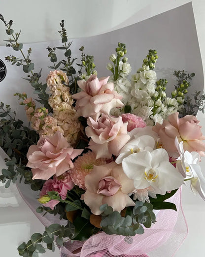 Elegant arrangement of seasonal flowers in ivory, rosy, and peachy shades, packaged in a signature presentation style for luxury and sophistication