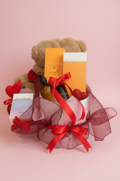 Gift basket with teddy bear, EGOYA products, and red ribbons on a table.