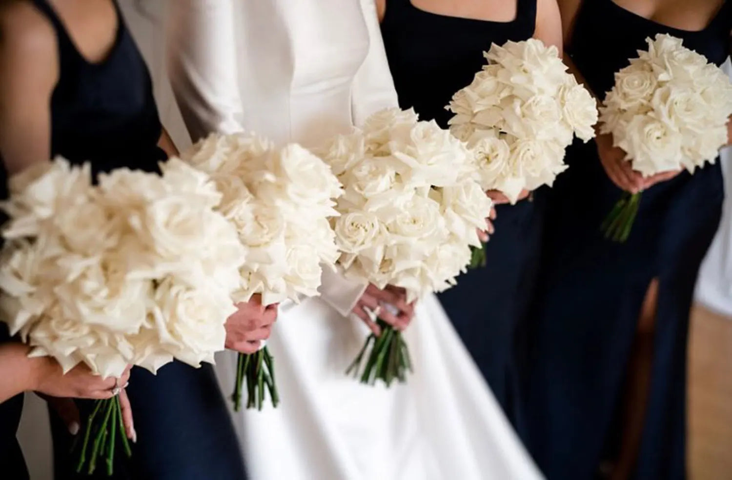 Elegant bridal bouquets lined up, featuring white roses, bridesmaids in navy blue and bride in the centre wearing white